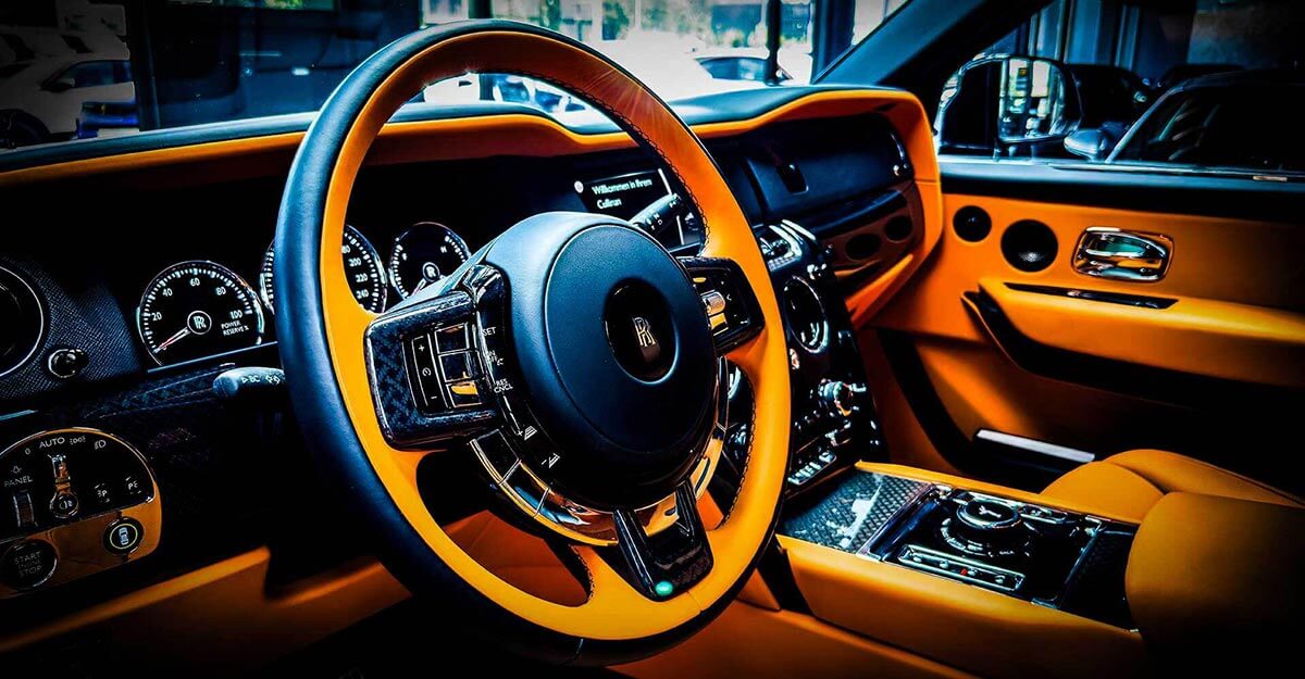 Nahaufnahme vom Innenraum des Rolls Royce Cullinan in orange und schwarz. Lenkrad im Fokus.